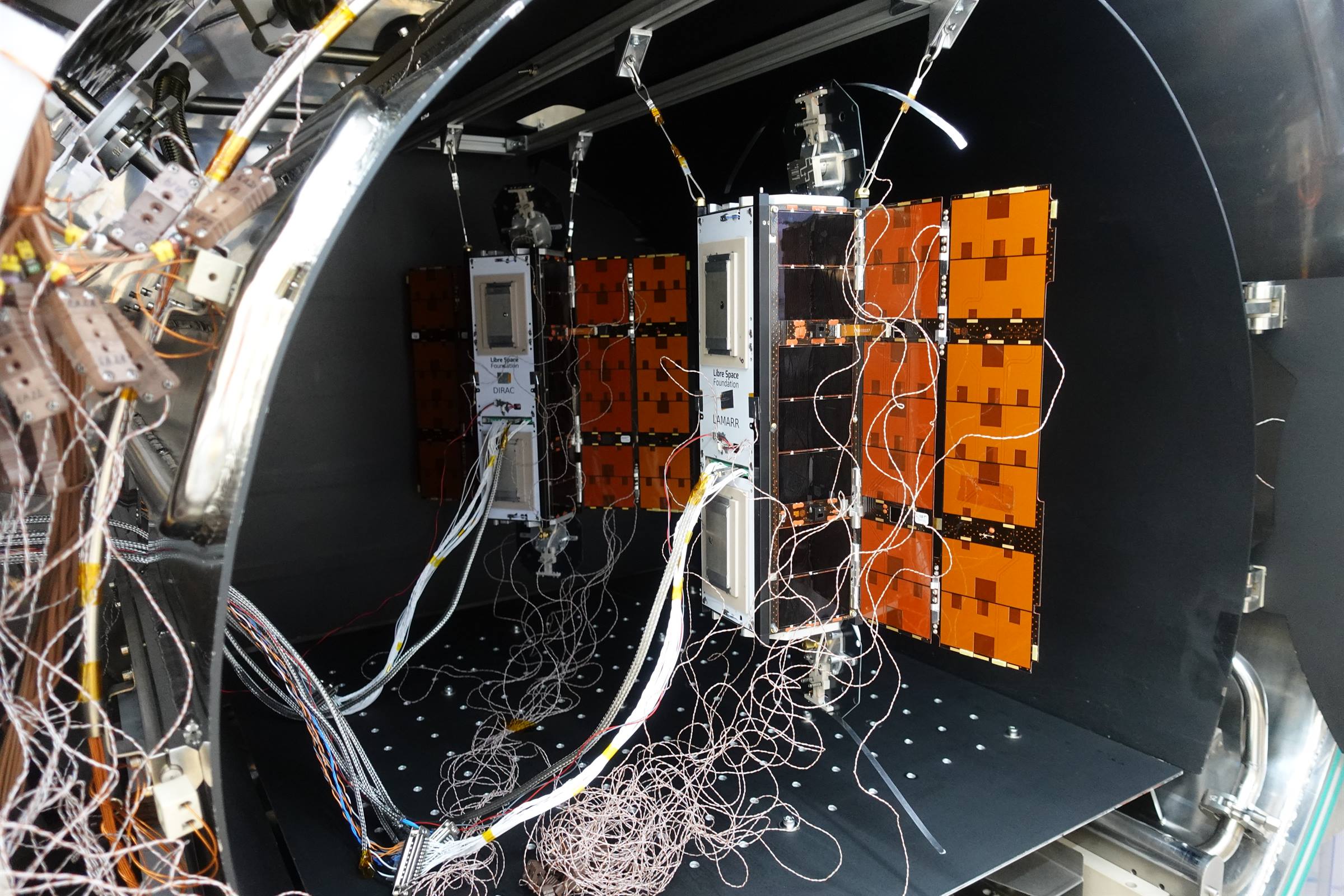 PHASMA-DIRAC and PHASMA-LAMARR CubeSats suspended inside a thermal-vacuum chamber, solar panels deployed and wired with thermocouples